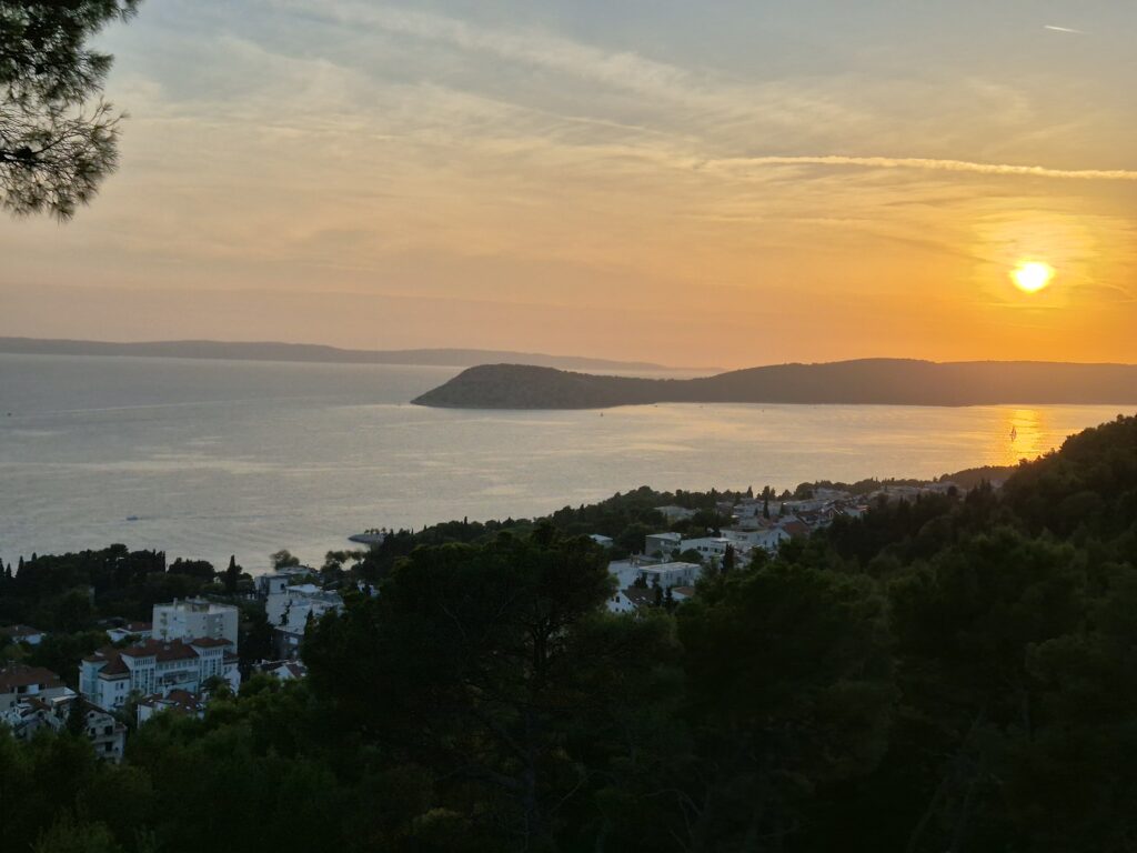 Panoramic view of Split from Marjan Hill, featuring the city’s terracotta rooftops, the Adriatic Sea, and nearby islands under a clear blue sky during the sunset.