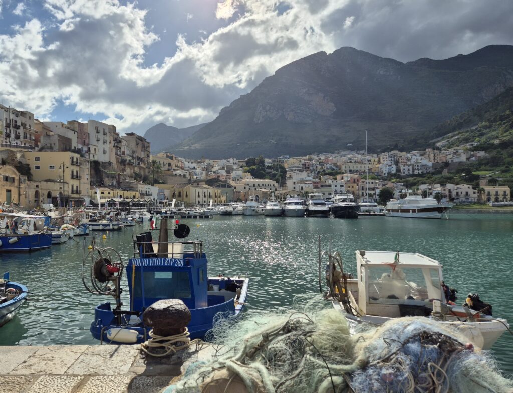 Castellammare del Golfo Marina: A vibrant view of the Castellammare del Golfo marina, showcasing colorful fishing boats gently floating in the crystal-clear waters, framed by a picturesque backdrop of historic buildings and lush green hills.