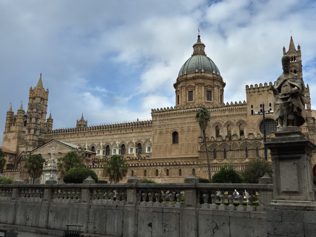 The stunning Palermo Cathedral, showcasing a blend of Norman, Gothic, and Baroque architecture, with intricate details and a majestic façade, set against a blue sky.