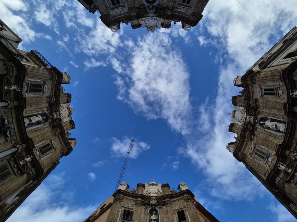 A lively view of Quattro Canti, Palermo’s iconic Baroque square, featuring four beautifully detailed buildings at each corner, with bustling city life and historic charm all around.